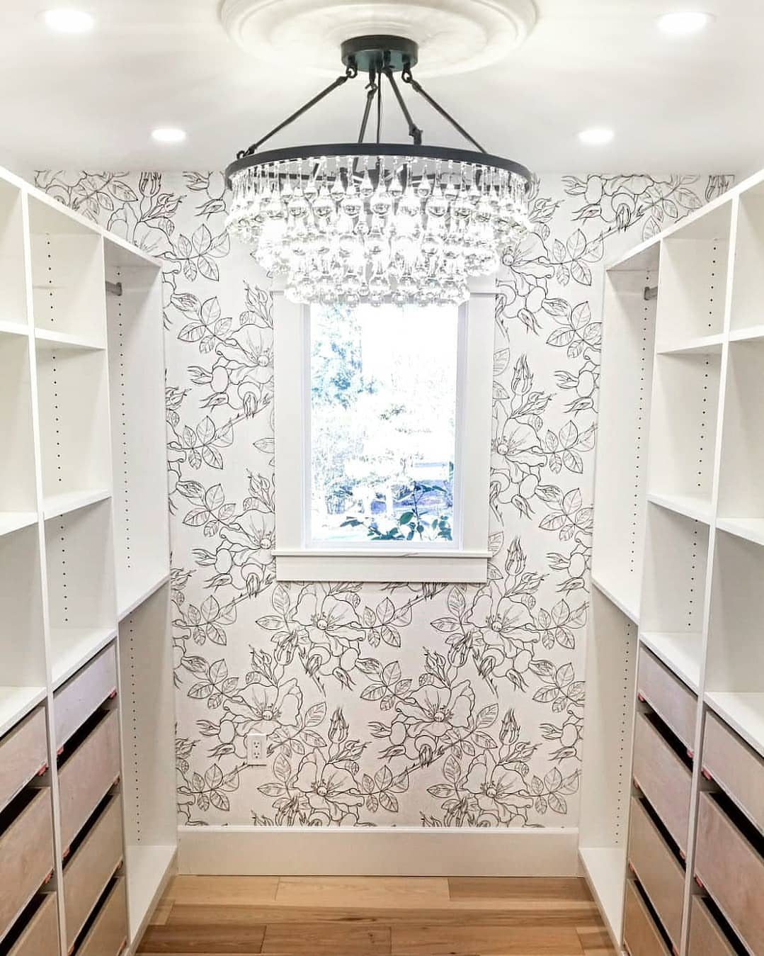 Floral patterned wallpaper on the back wall of a narrow white closet with chandelier