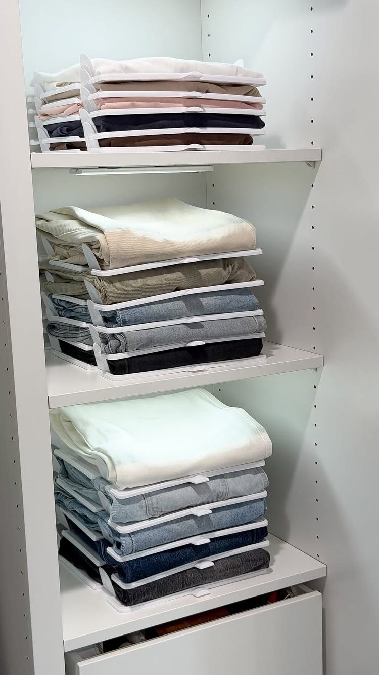 Folded clothes organized with white plastic dividers on white narrow closet shelves.