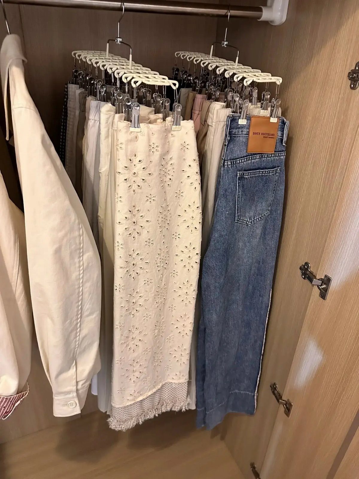 White slim hangers holding skirts and jeans on a metal closet rod.