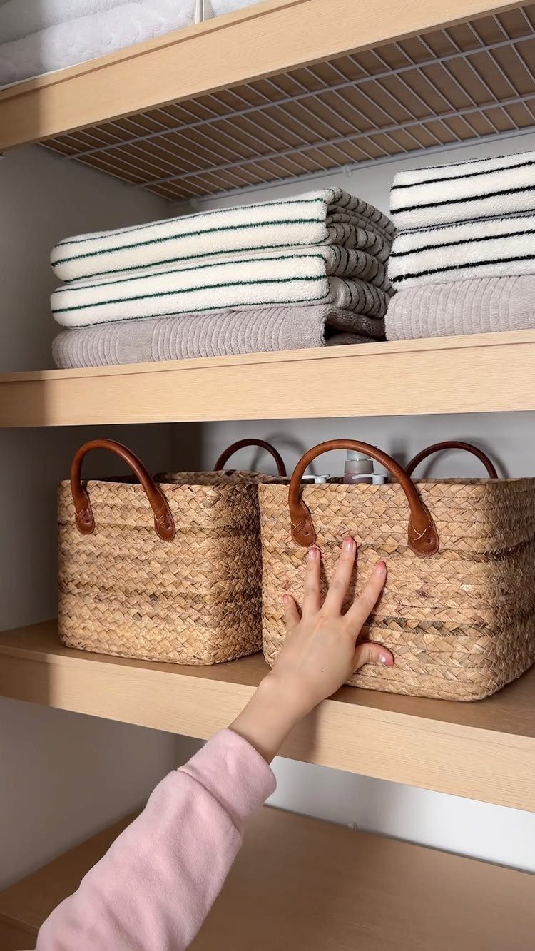Woven seagrass baskets and folded towels on light wood closet shelving.