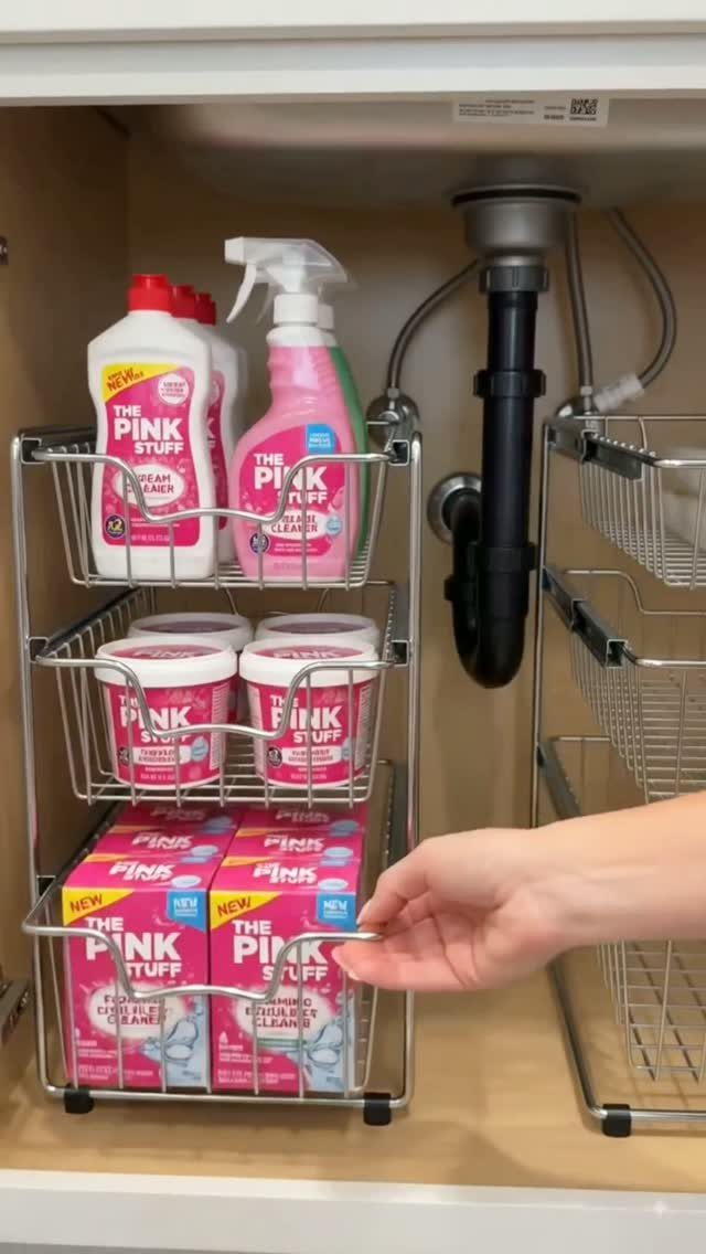 Pink cleaning supplies organized on a metal wire rack under a bathroom sink.