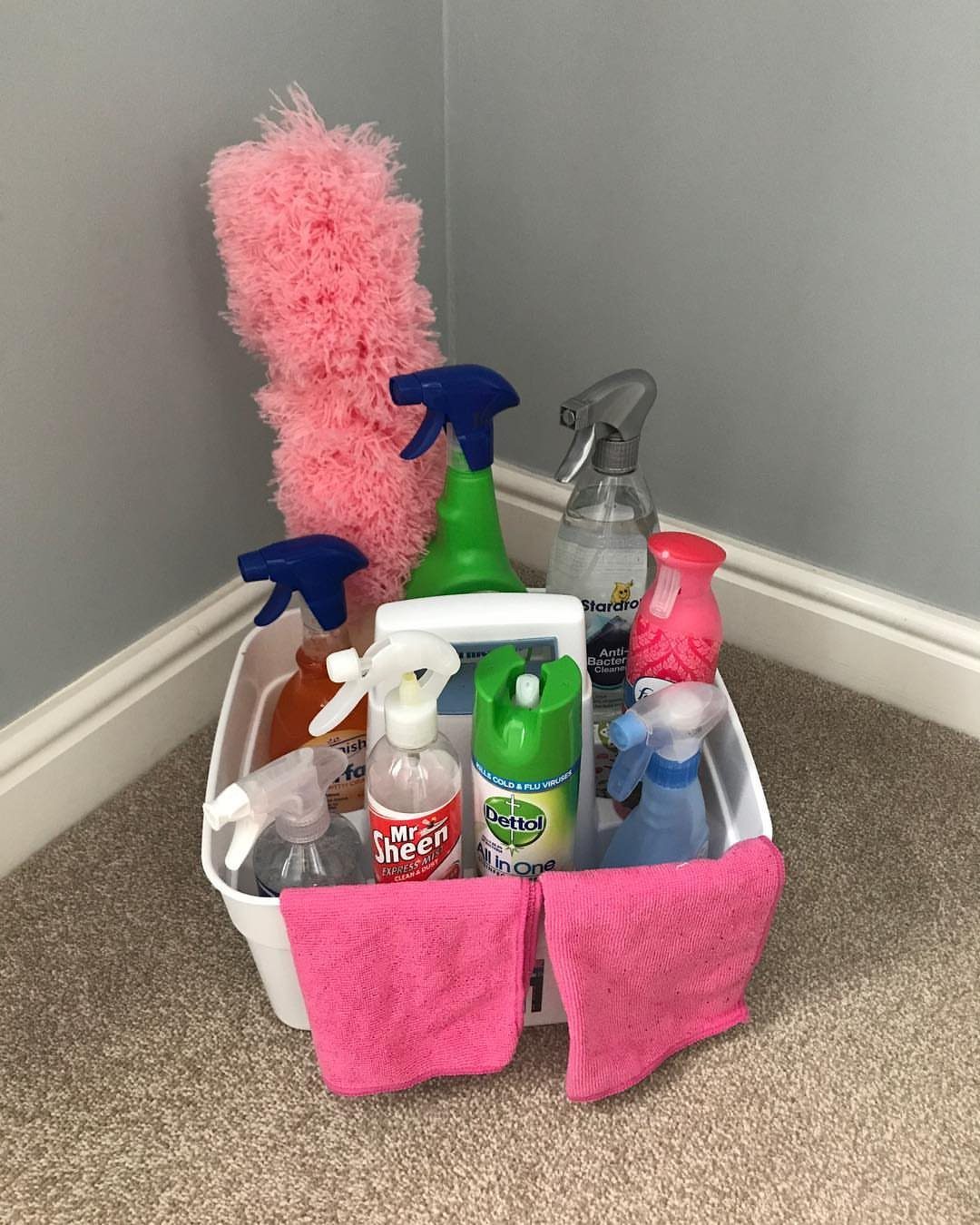 White cleaning caddy containing spray bottles, a pink duster, and pink cleaning cloths.