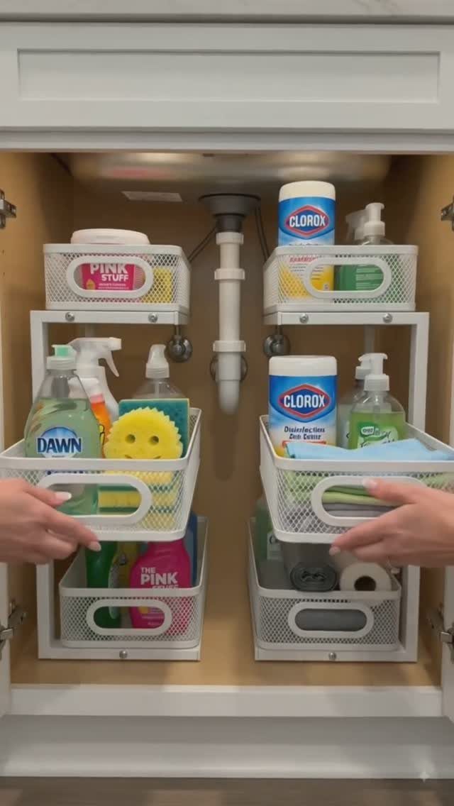 Under-sink cabinet with white mesh pull-out drawers holding various cleaning supplies and sponges.