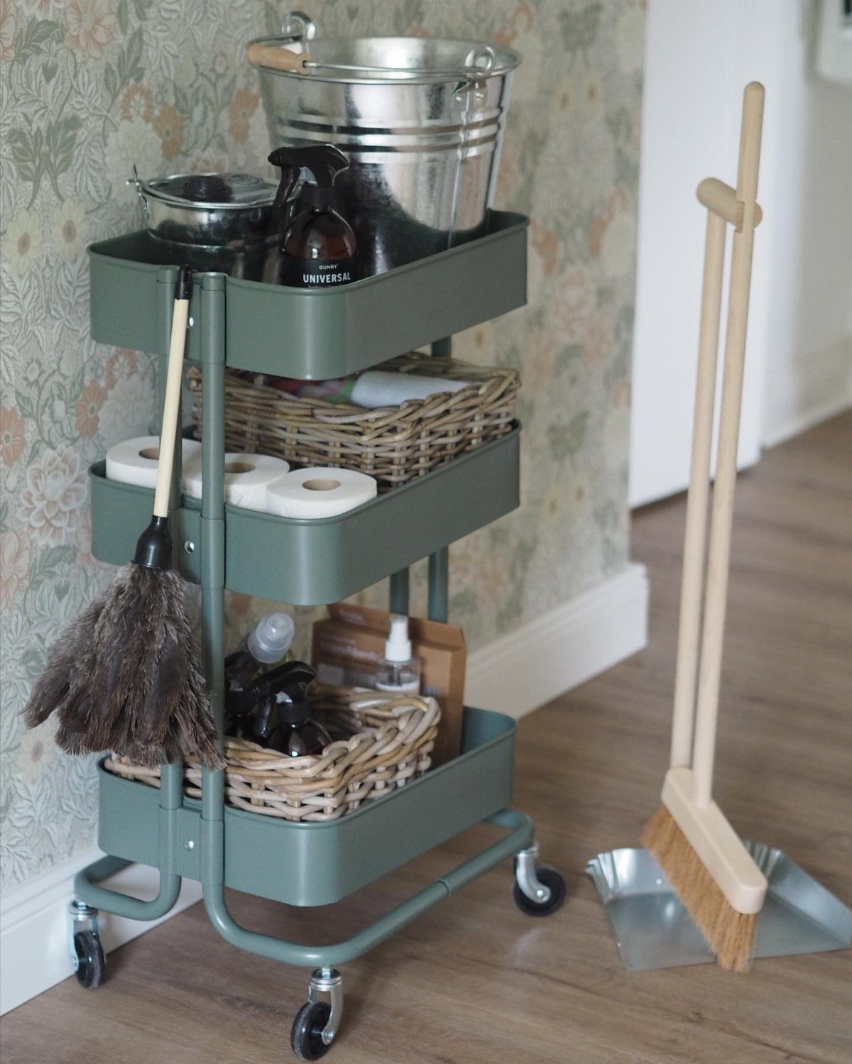 Green rolling utility cart organized with cleaning supplies, buckets, and baskets.