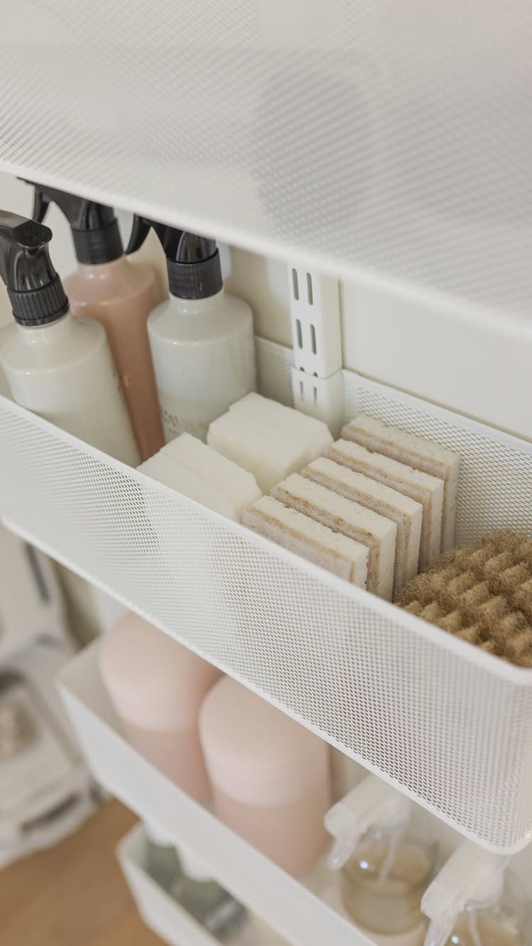 White mesh bins holding cleaning sprays and sponges inside an organized white closet.