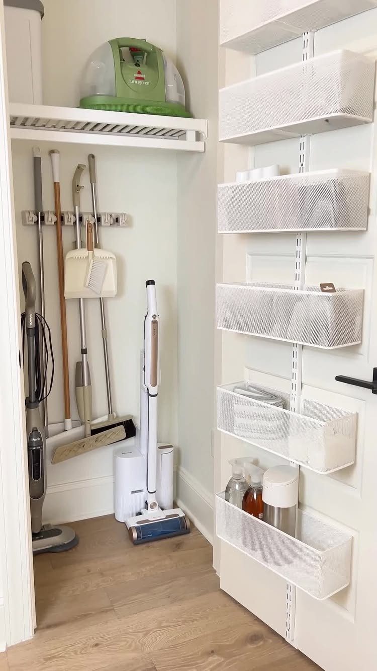 Narrow cleaning closet with brooms, a vacuum, and a door-mounted mesh organizer.