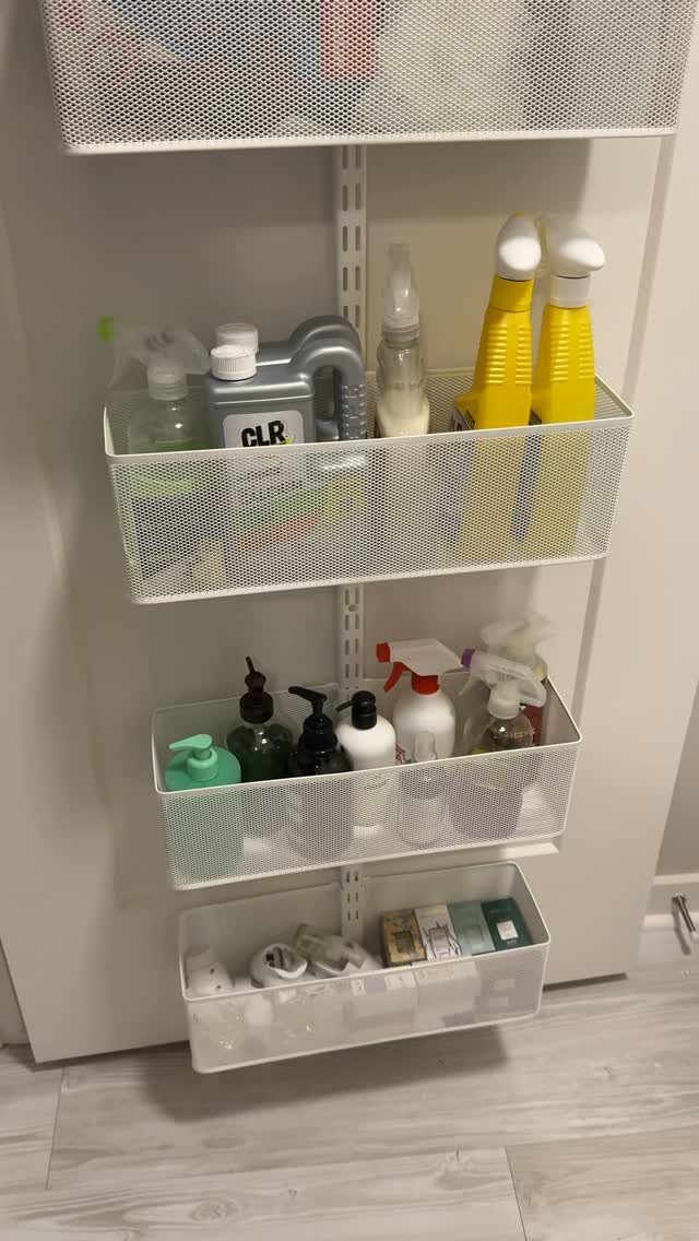 White wire mesh baskets on a wall track holding various cleaning spray bottles.