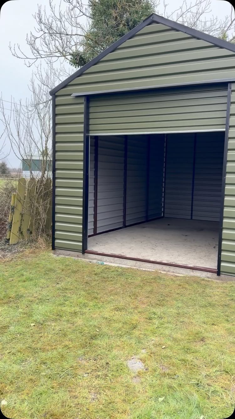 Green metal storage shed with an open roll-up door on a grassy lawn