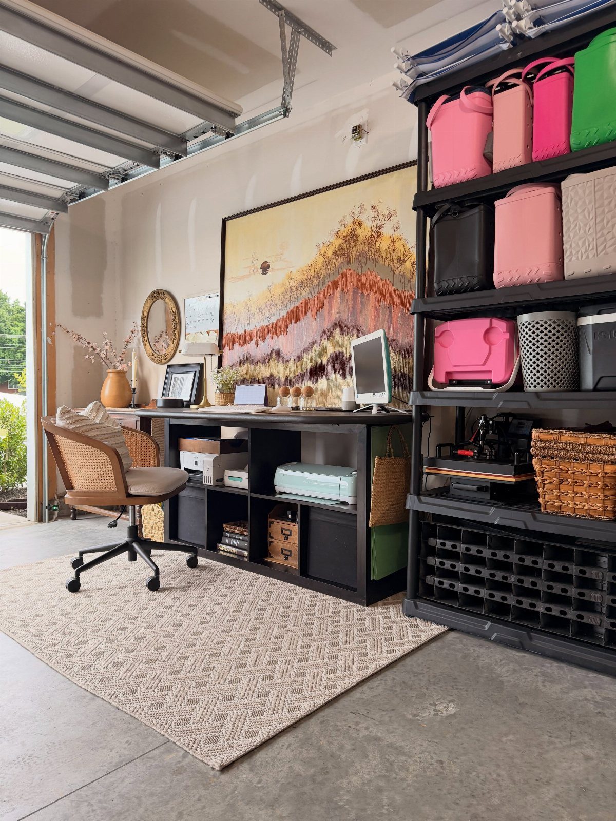 Garage office setup with a black desk, tan chair, and large landscape painting.