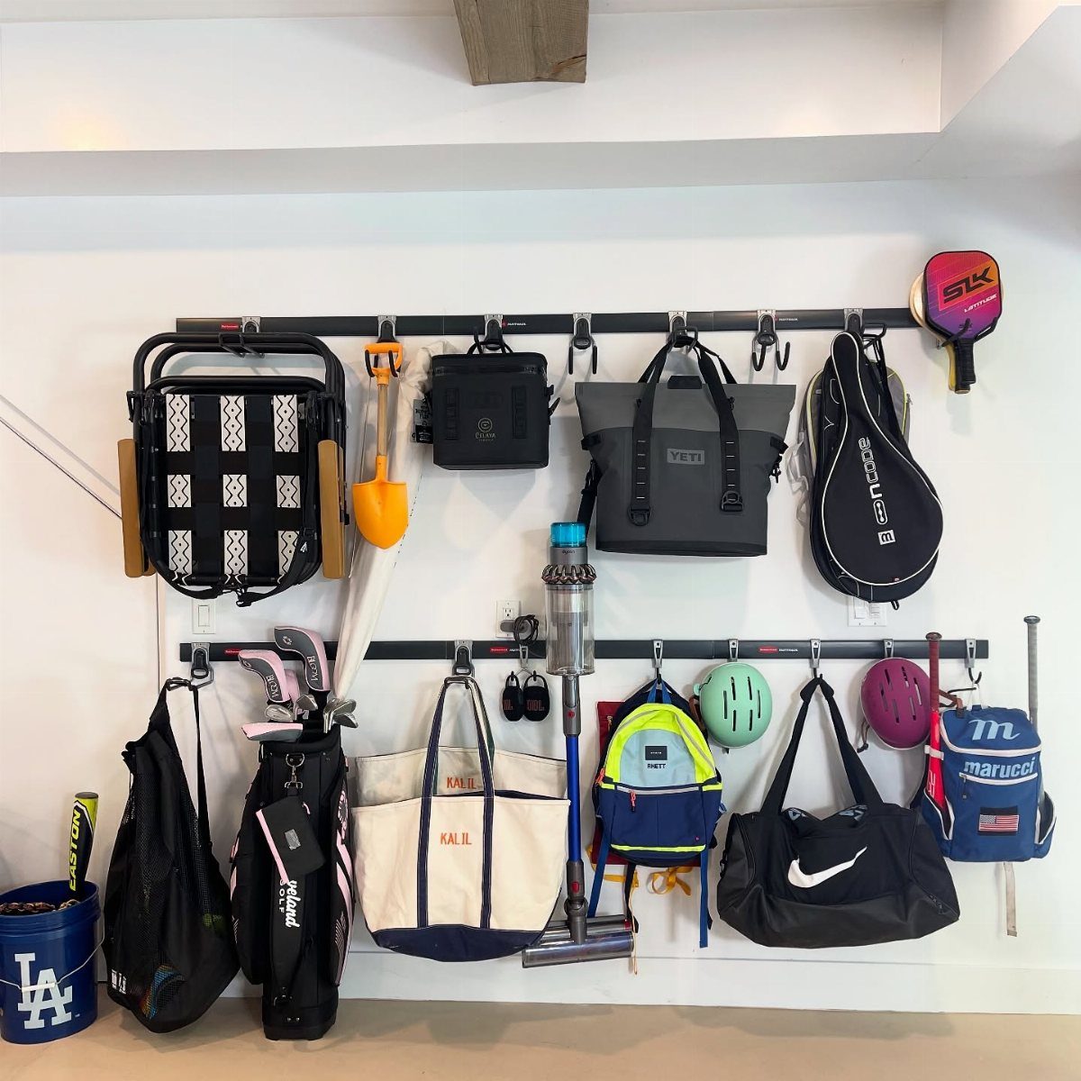 Sports equipment and cleaning tools hanging from black rails on a white garage wall.