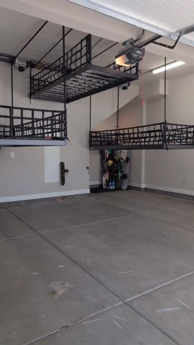 Black metal overhead storage racks suspended from a garage ceiling above a concrete floor.