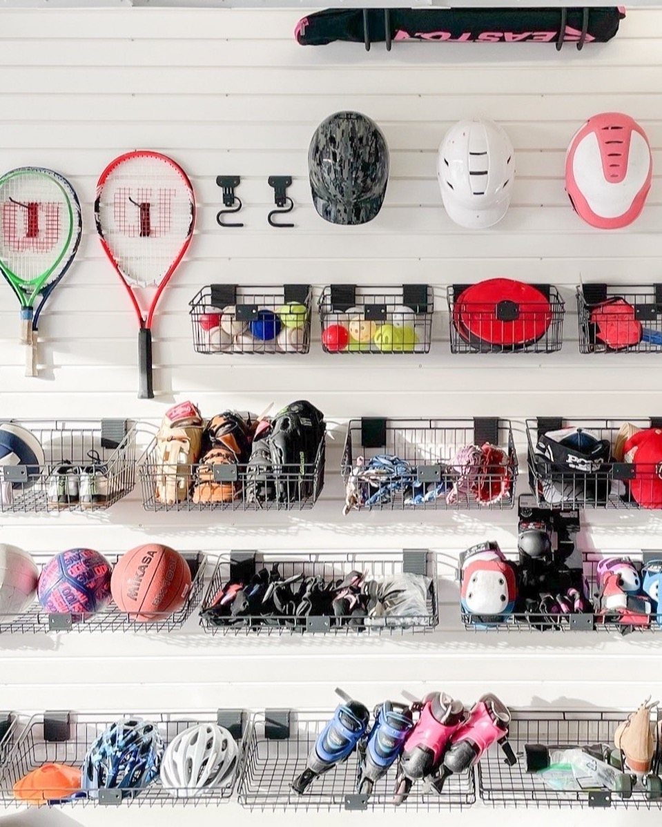 Sports equipment organized on a white wall using wire baskets and hooks.