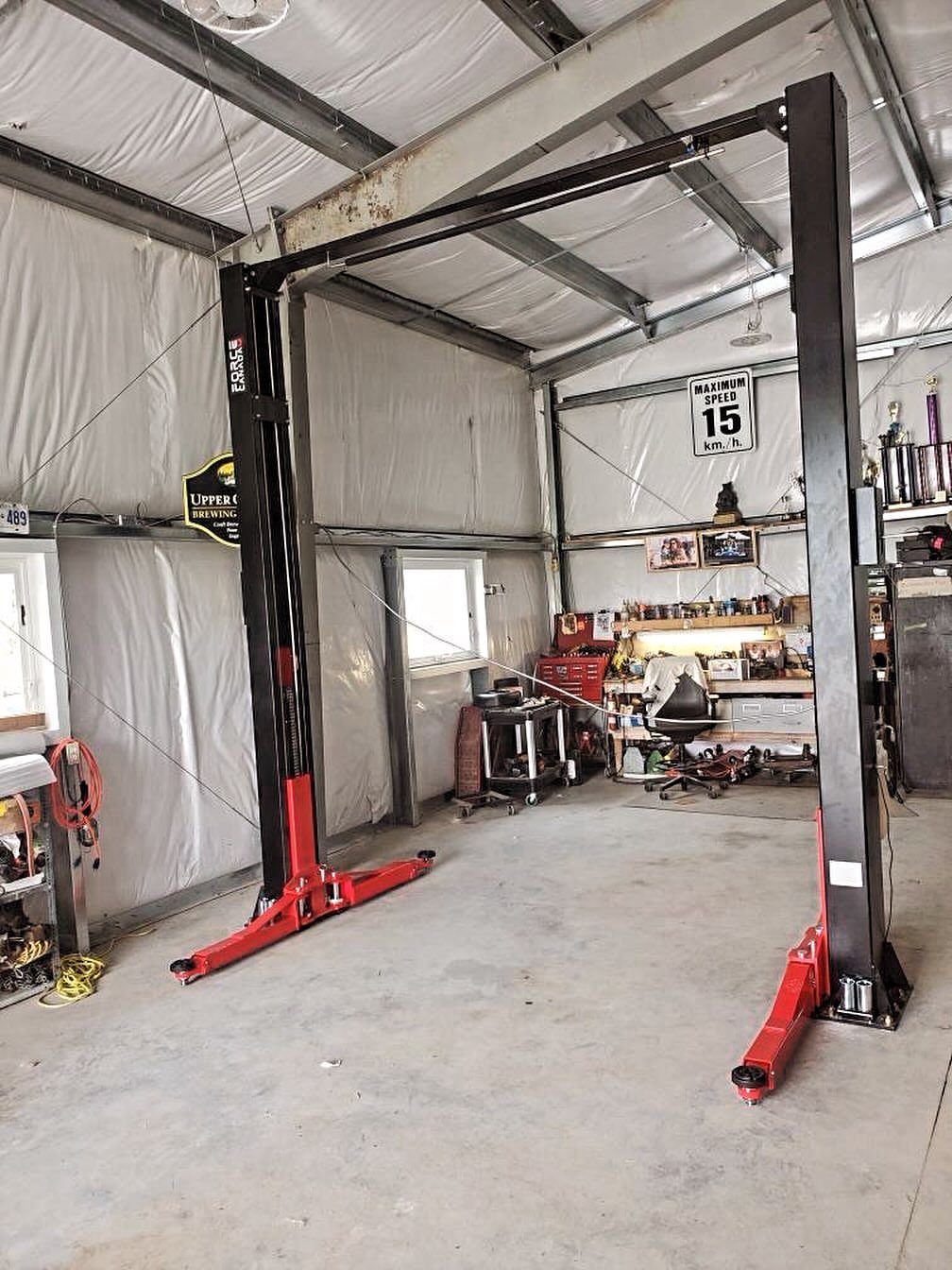 Two-post automotive vehicle lift installed in a white walled garage with concrete flooring.