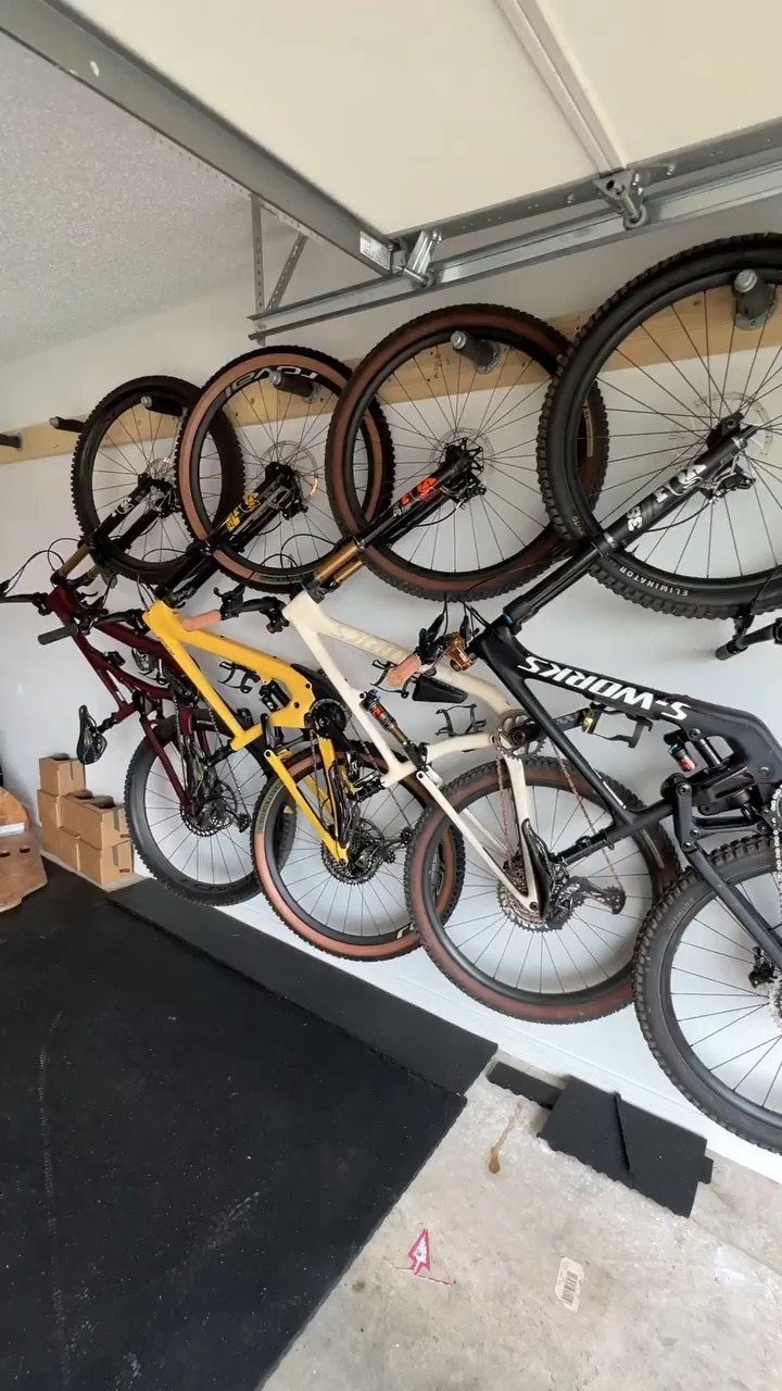 Four mountain bikes mounted vertically on a white garage wall using black racks.