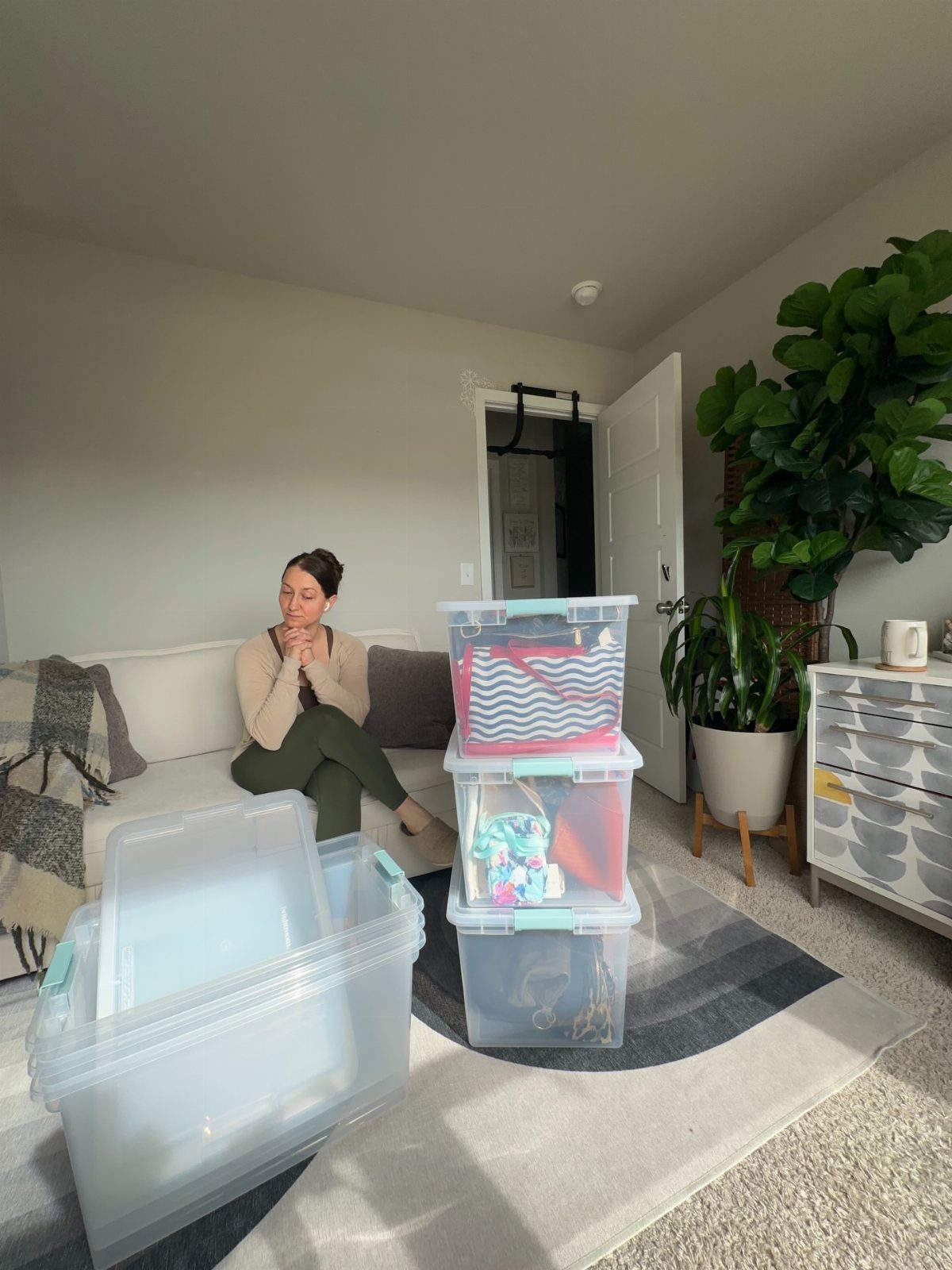 Clear plastic storage bins stacked in a living room with a woman sitting nearby.