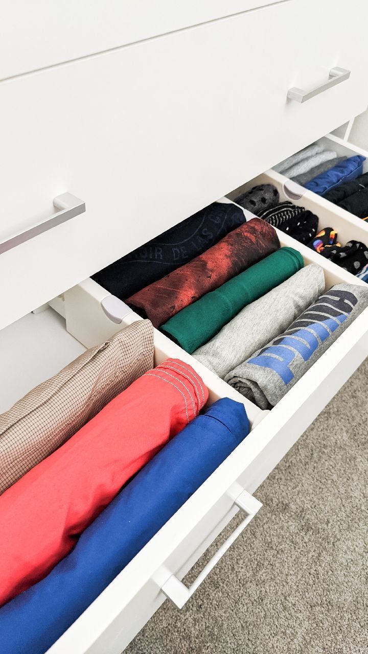 White dresser drawer with dividers holding neatly folded colorful t-shirts.