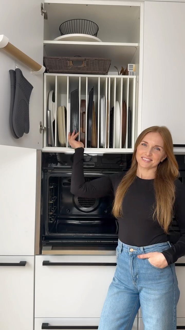 Woman opening a pull-out kitchen drawer containing vertically organized baking sheets and pans.