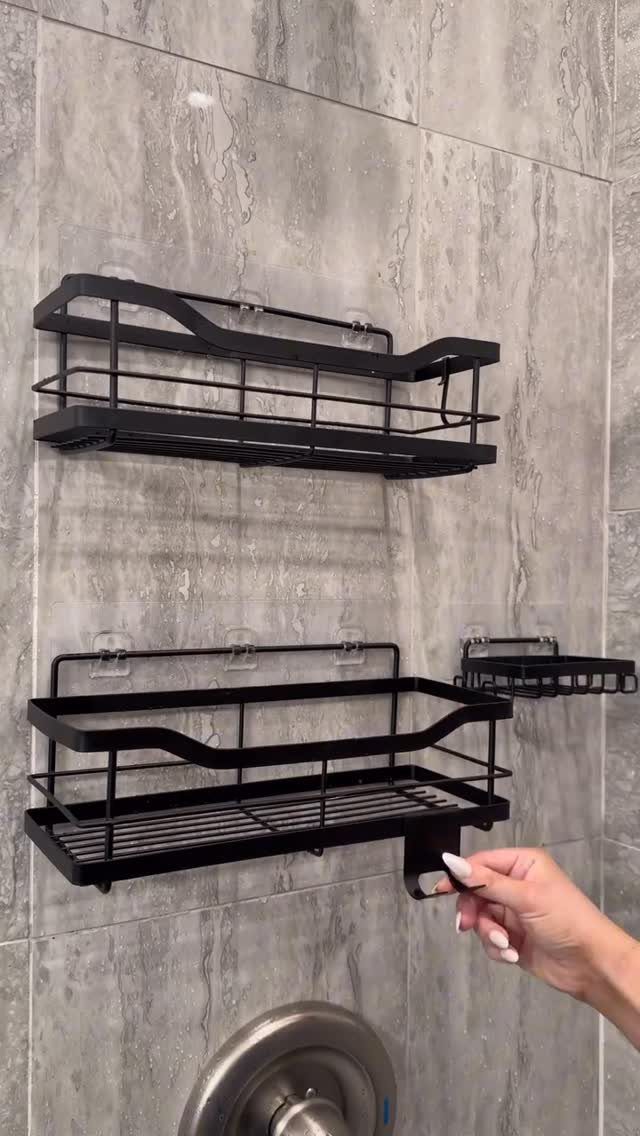 Black metal wire shower caddies mounted on a grey marbled tile bathroom wall.