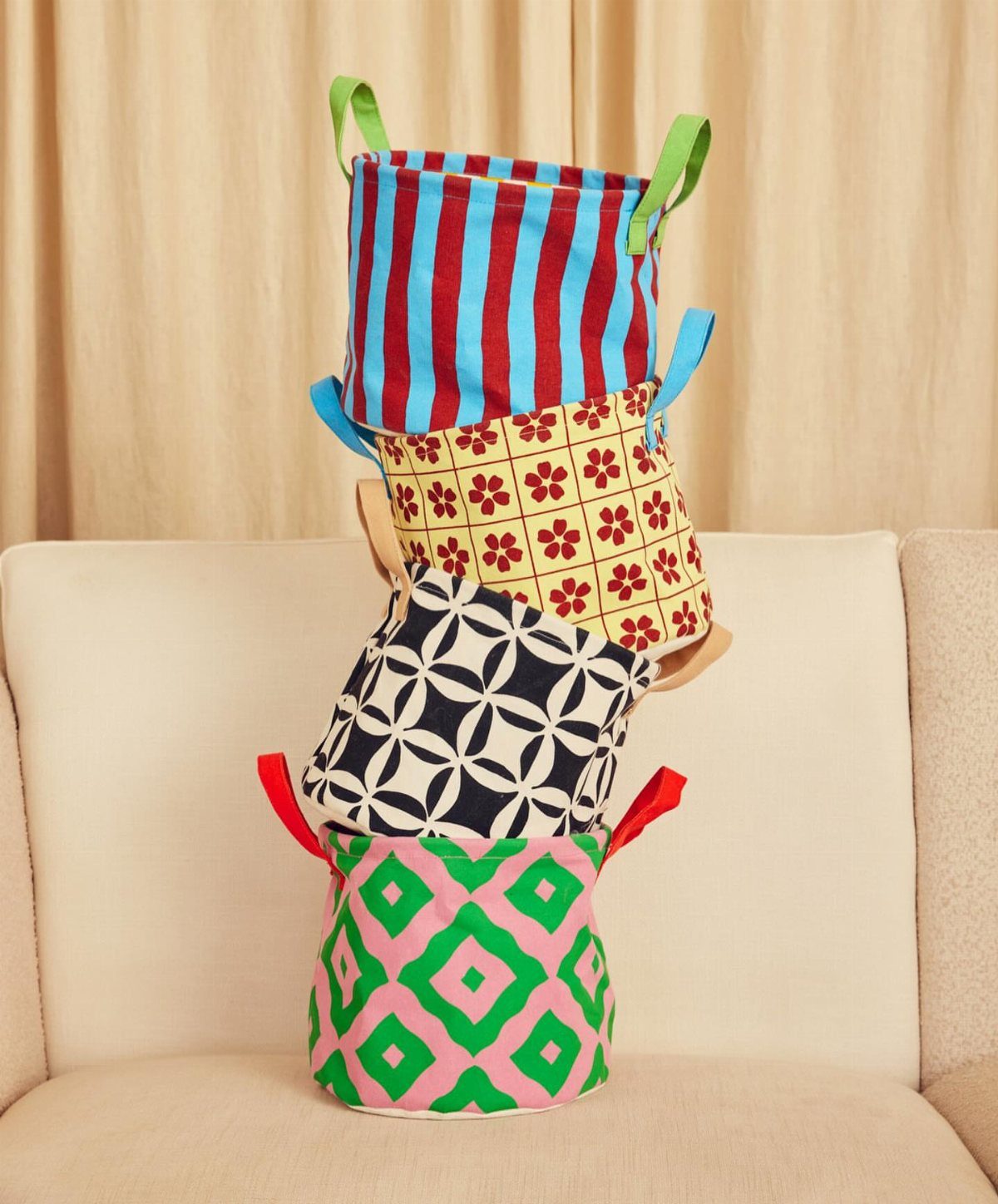 Four colorful patterned fabric storage baskets stacked on a beige sofa.