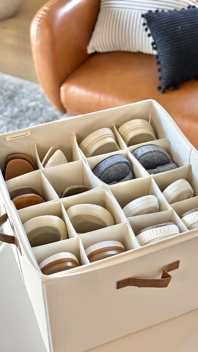 Cream fabric storage box with dividers organizing various pairs of slippers and shoes.