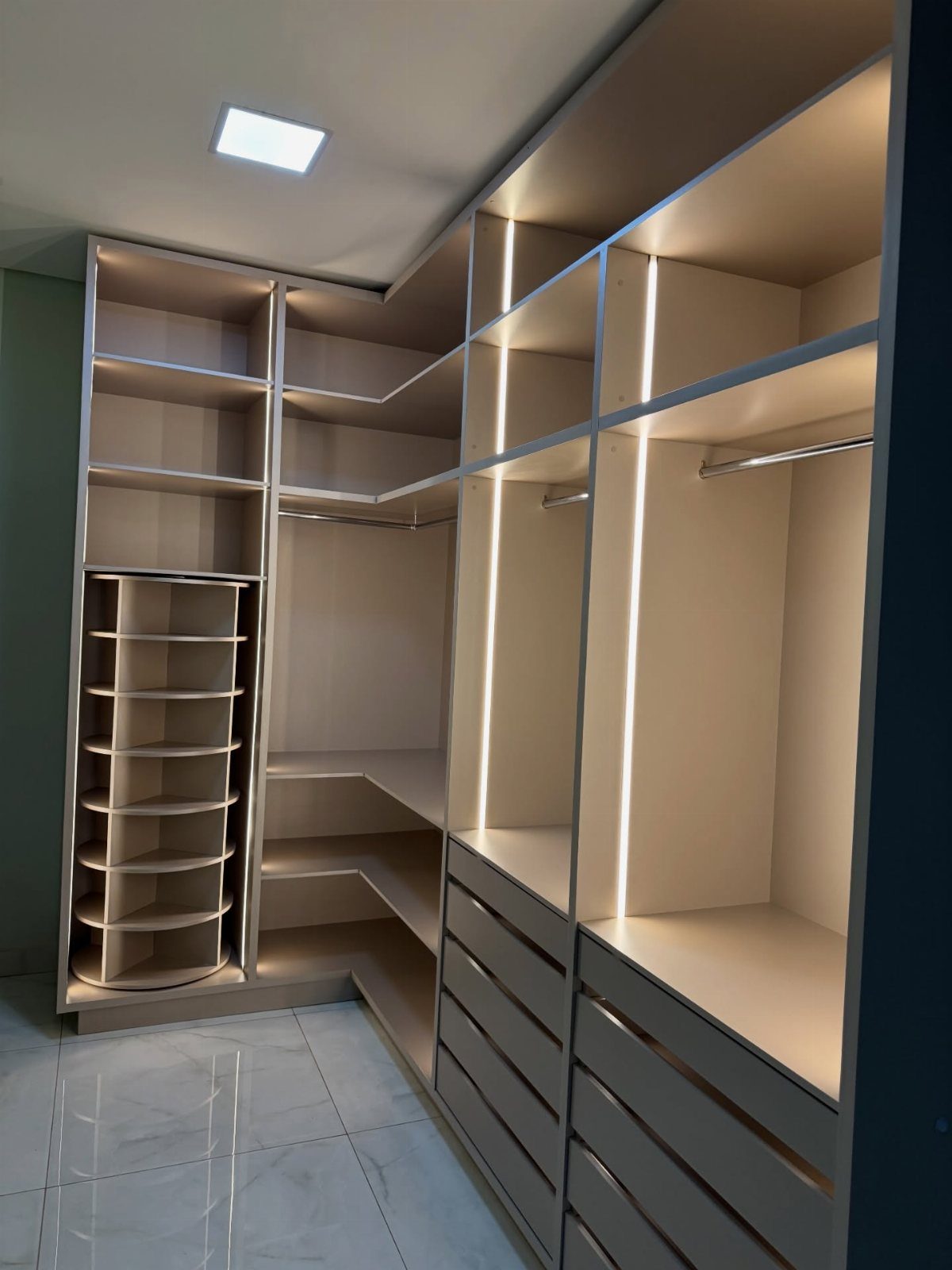 Modern reach-in closet with beige shelves, drawers, and integrated vertical LED lighting.