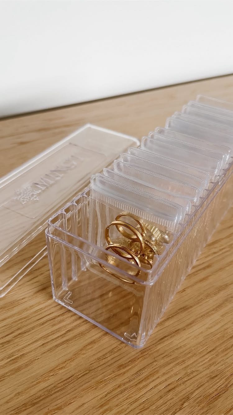 Gold rings in small plastic bags inside a clear acrylic jewelry organizer.