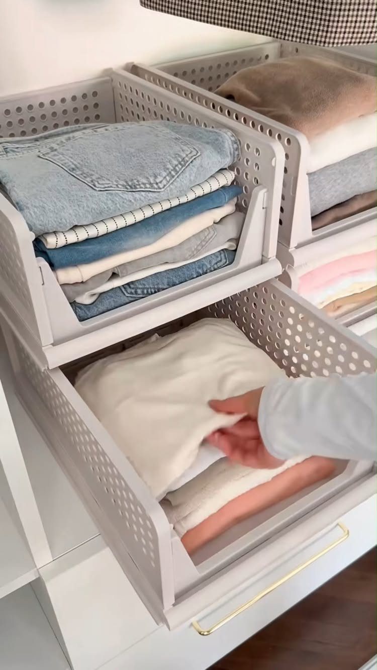 White perforated storage bins holding folded clothes inside a small reach-in closet.