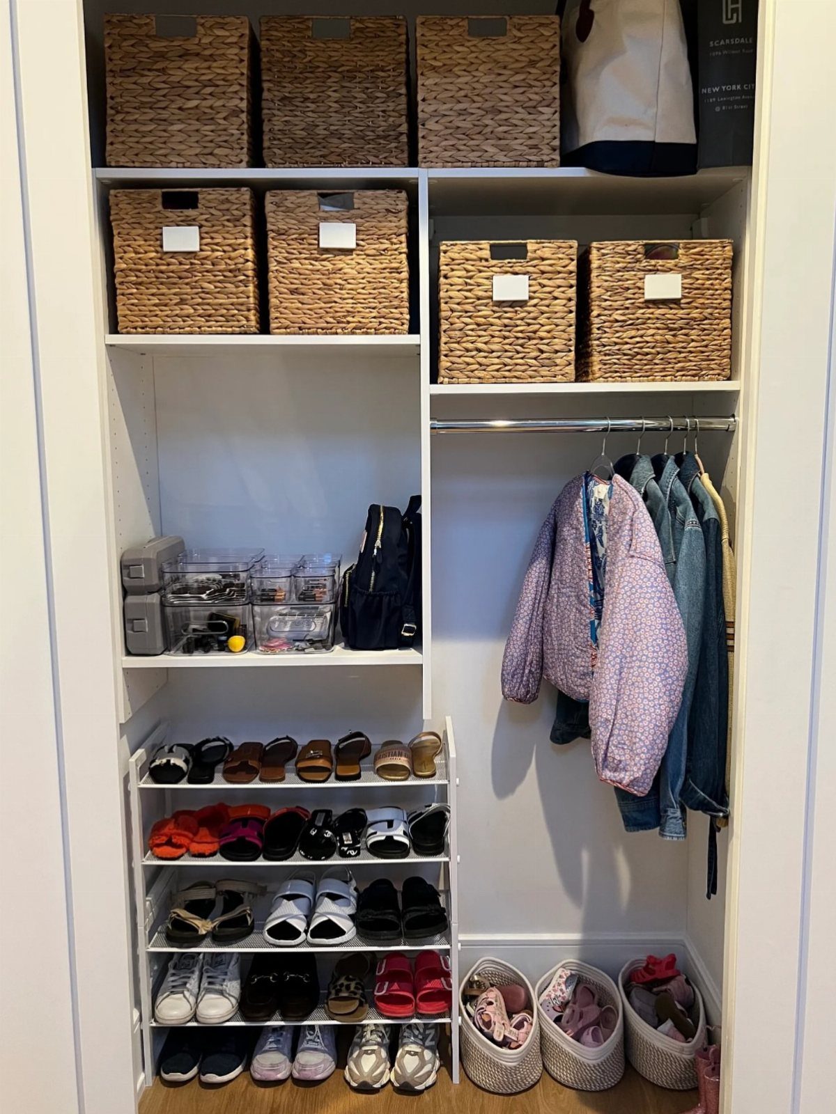 White reach-in closet with woven baskets, hanging clothes, and a tiered shoe rack.