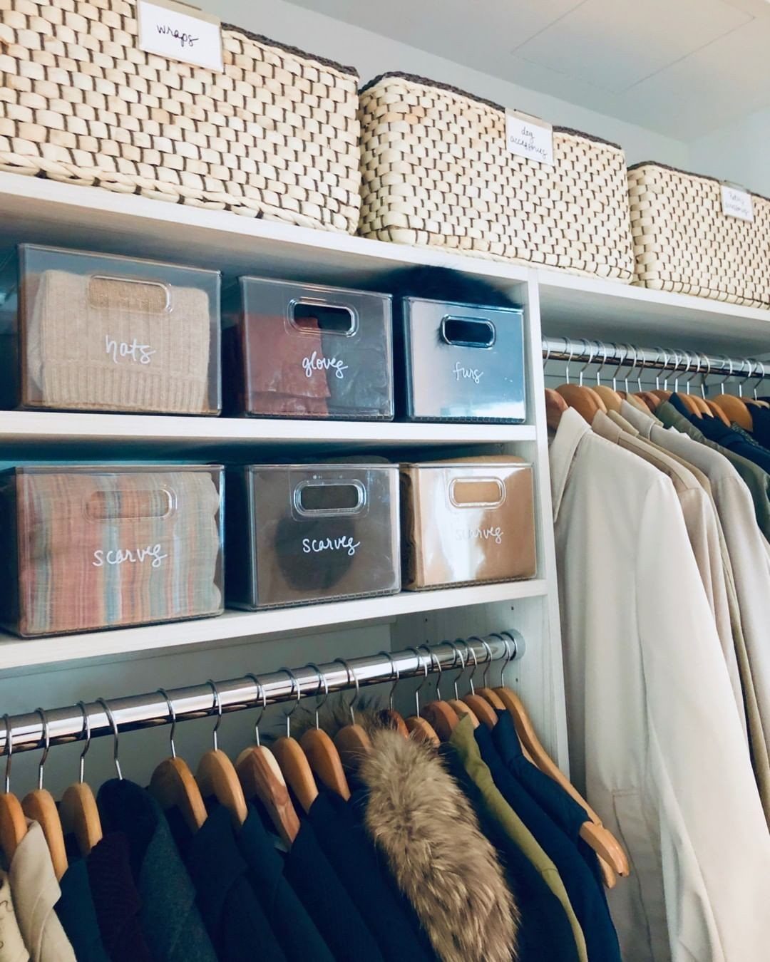 White closet shelves with woven baskets and labeled clear plastic storage bins.