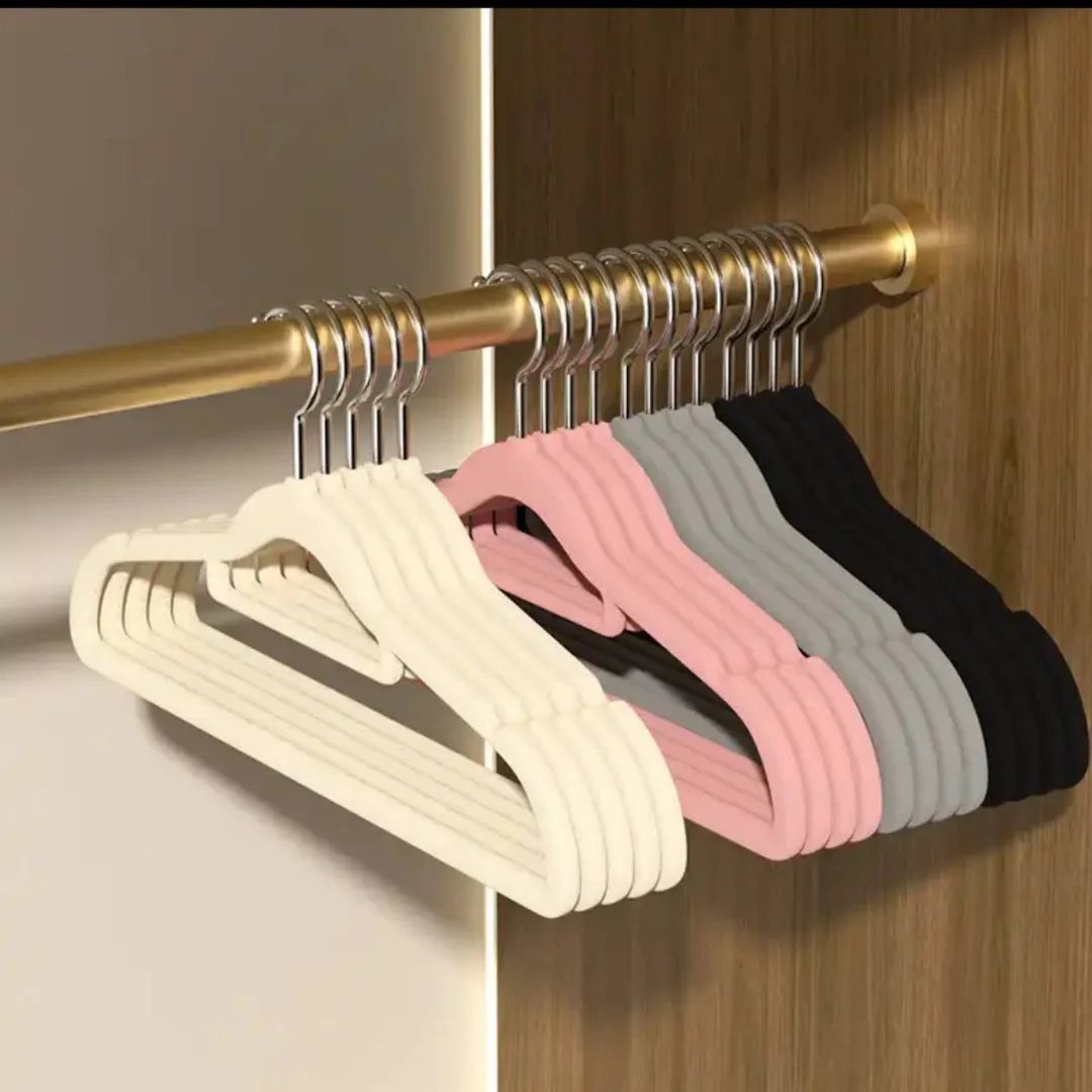 Slim velvet hangers in various colors hanging on a gold metal closet rod.