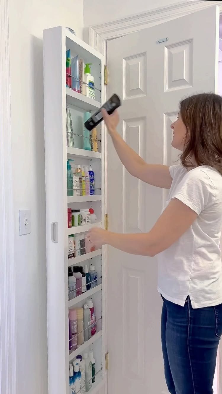 Woman organizing toiletries in wire shelves attached to the inside of a cabinet door.