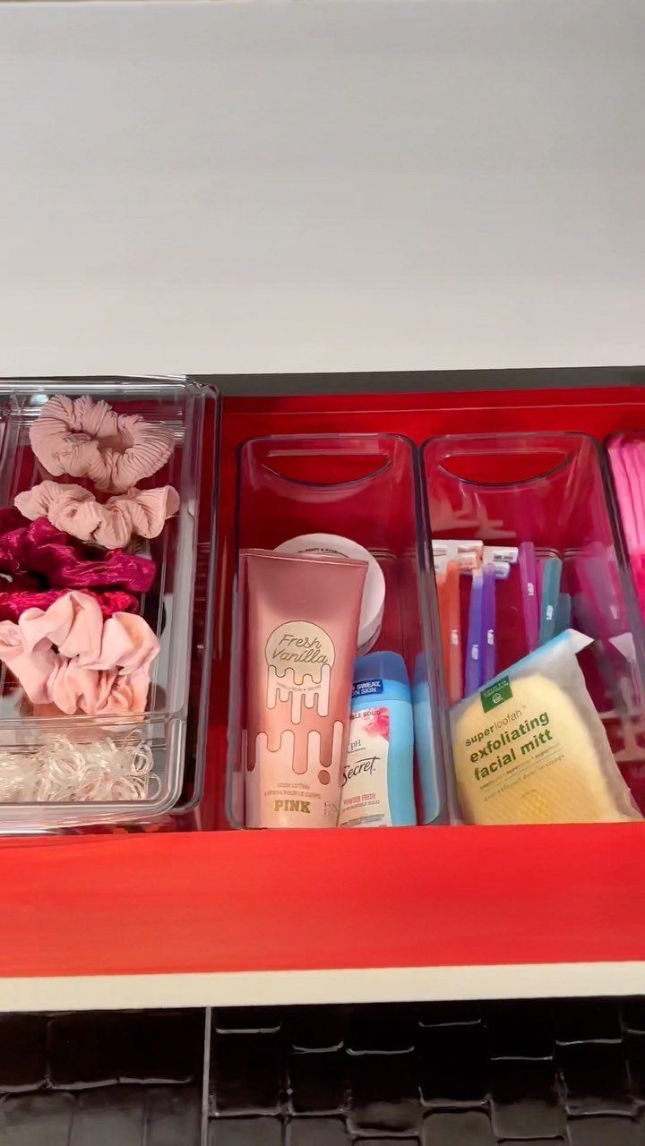 Red drawer with clear plastic bins organizing hair accessories and skincare products.