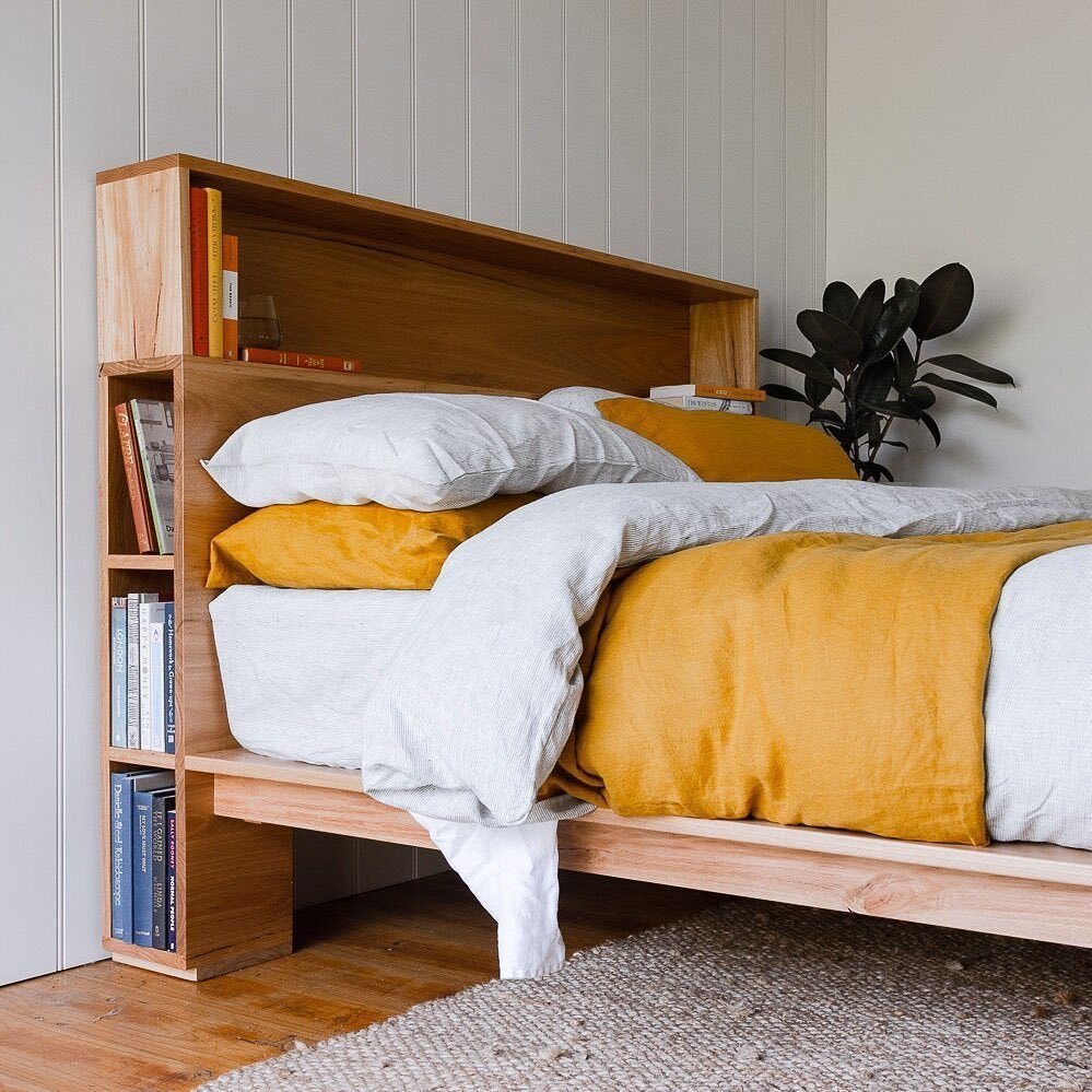 Wooden bed frame featuring a headboard bookshelf and side storage filled with books.
