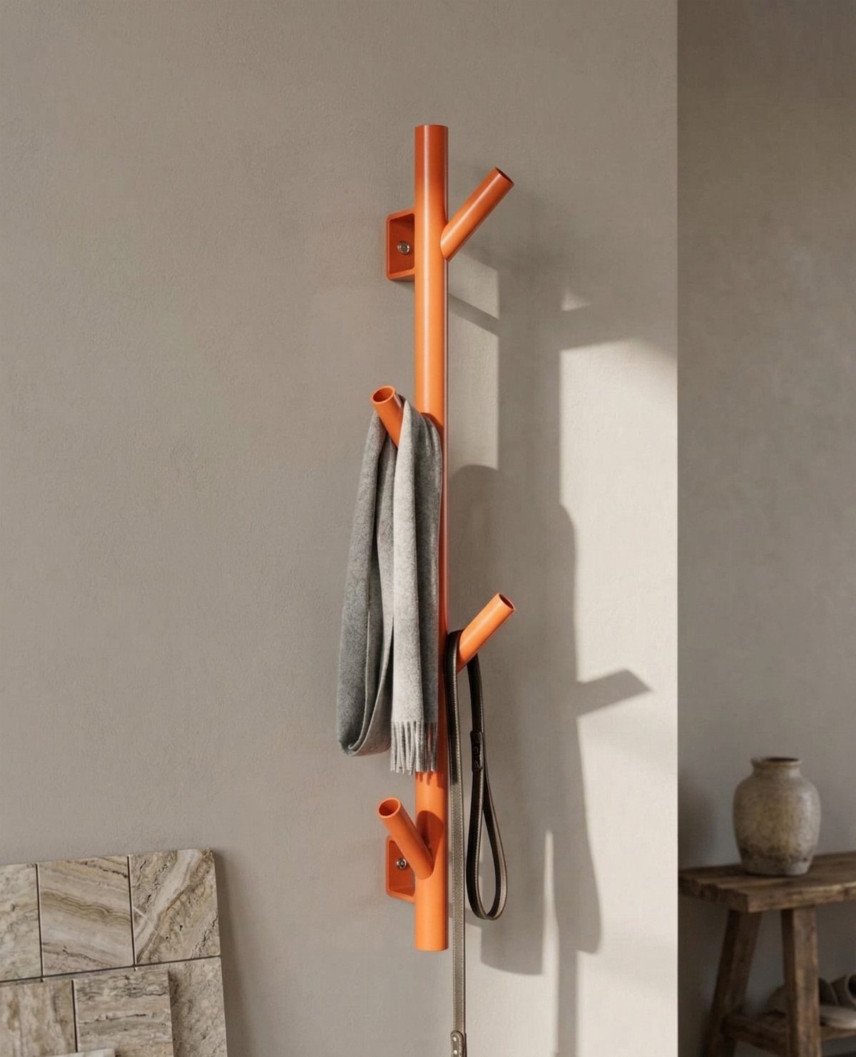 Orange sculptural wall hook rack holding a grey scarf and a dark strap.