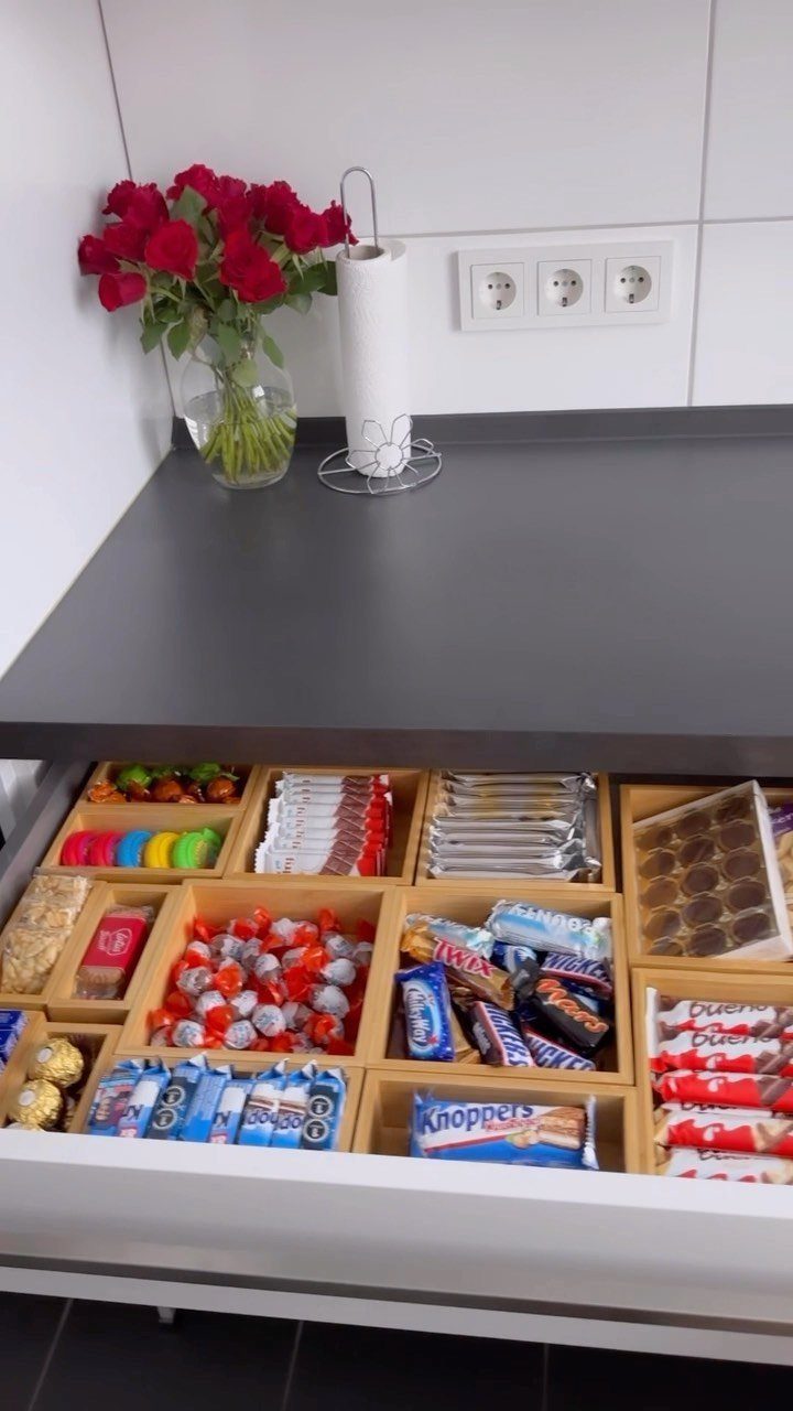 Wooden drawer dividers organizing various packaged snacks and candies in a kitchen drawer.