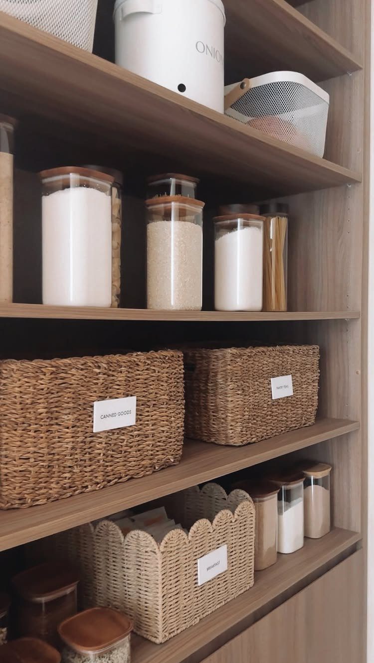 Clear glass jars with wooden lids storing grains on a wooden pantry shelf.