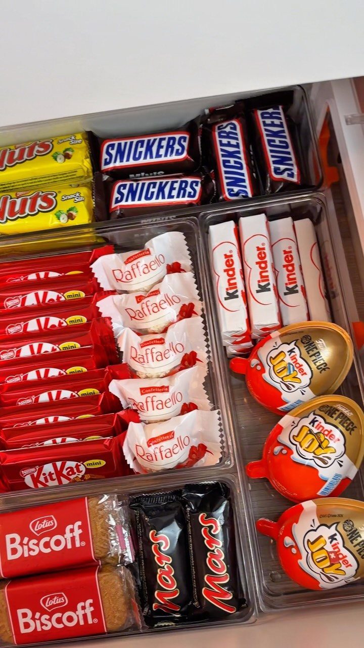 Organized kitchen drawer with clear dividers filled with assorted branded chocolate and biscuit snacks.