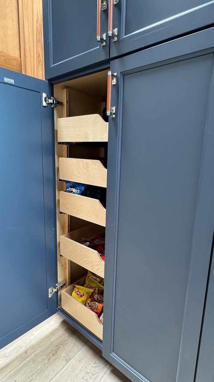Open blue kitchen cabinet with a vertical stack of wooden pull-out snack drawers.