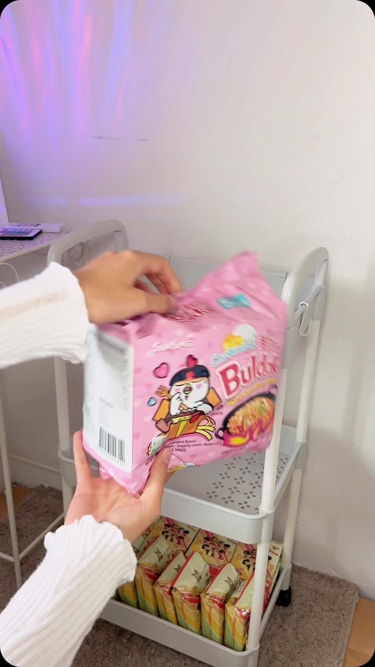 White rolling utility cart used as a snack station with instant noodle packages.