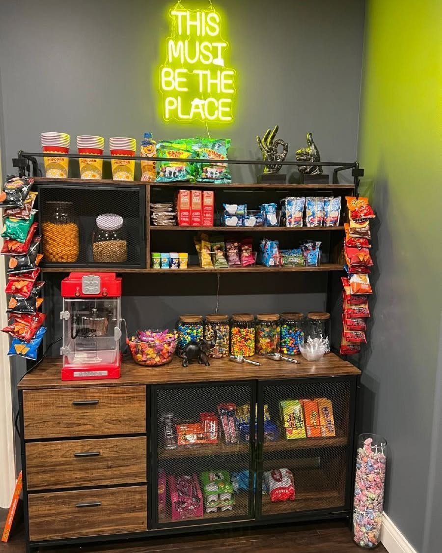 Home snack station with wooden cabinets, shelves of treats, and a yellow neon sign.