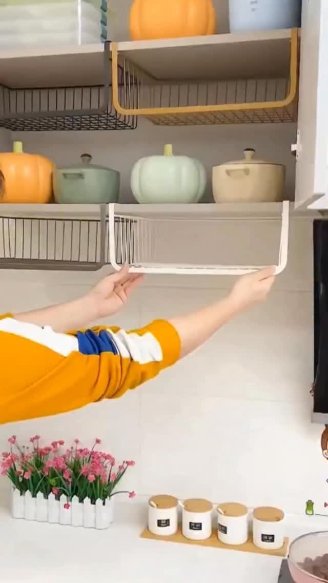 White wire under-shelf basket being installed beneath a kitchen shelf with ceramic pots.