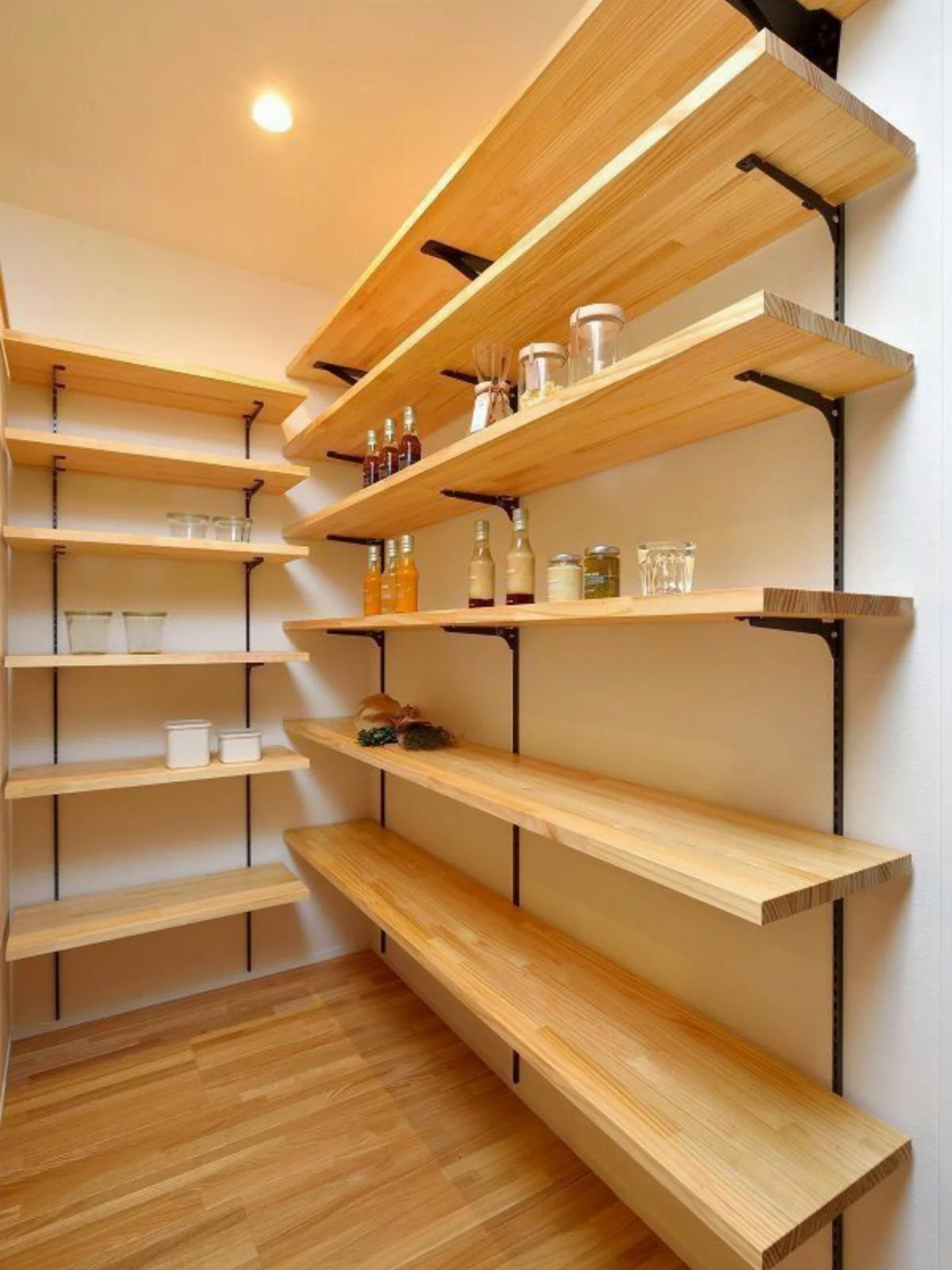 Wooden vertical wall shelves in a pantry holding glass jars and bottles.