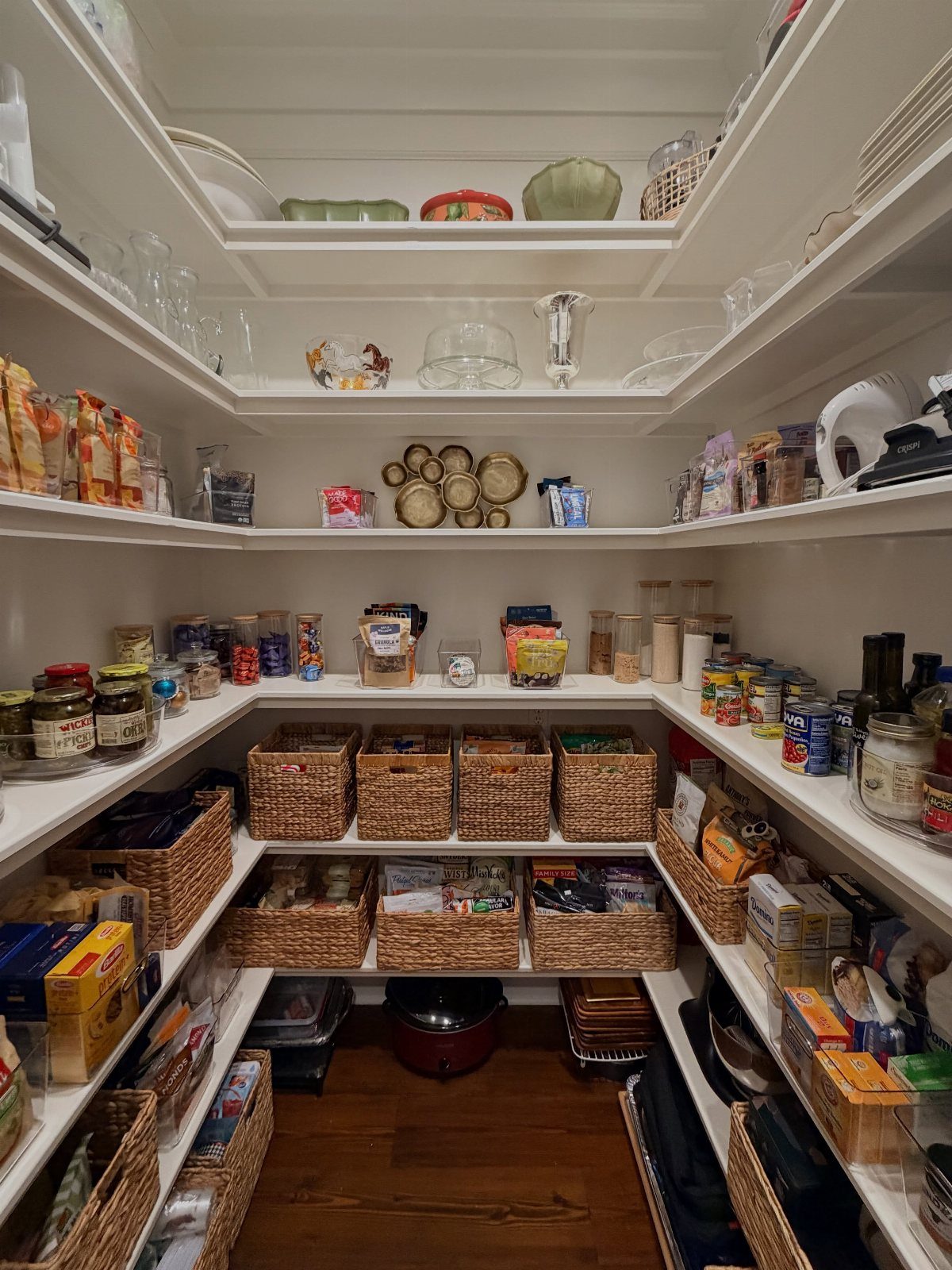 Organized walk-in pantry with white shelves and woven wicker baskets containing snacks.
