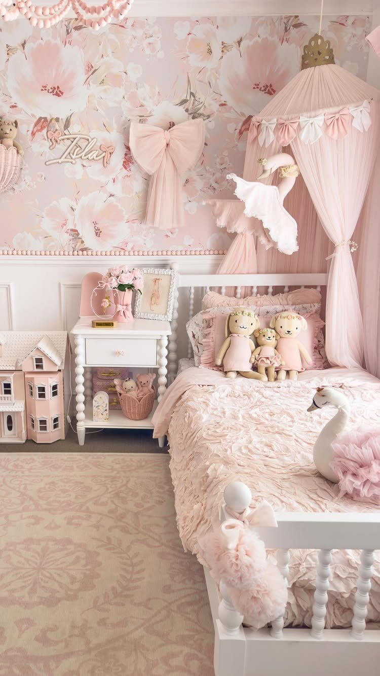 Pink floral wallpaper and a pink fabric canopy over a white toddler bed.