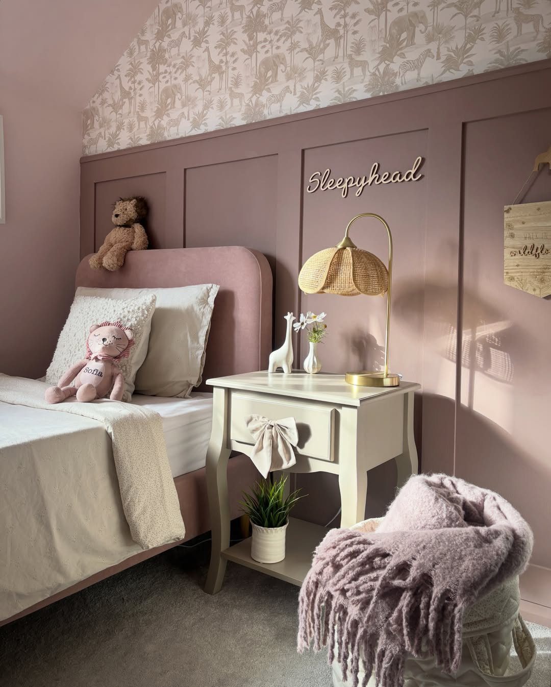 Mauve painted wood paneling and floral wallpaper in a toddler girl's bedroom.
