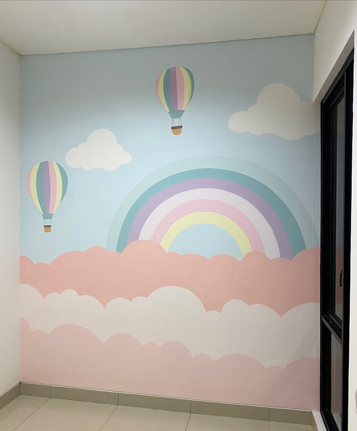 Pastel rainbow mural with hot air balloons and clouds on a blue wall.