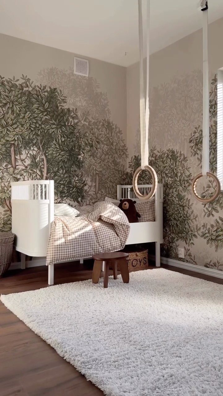 Toddler bedroom with a forest wall mural, white bed, and hanging ring swings.