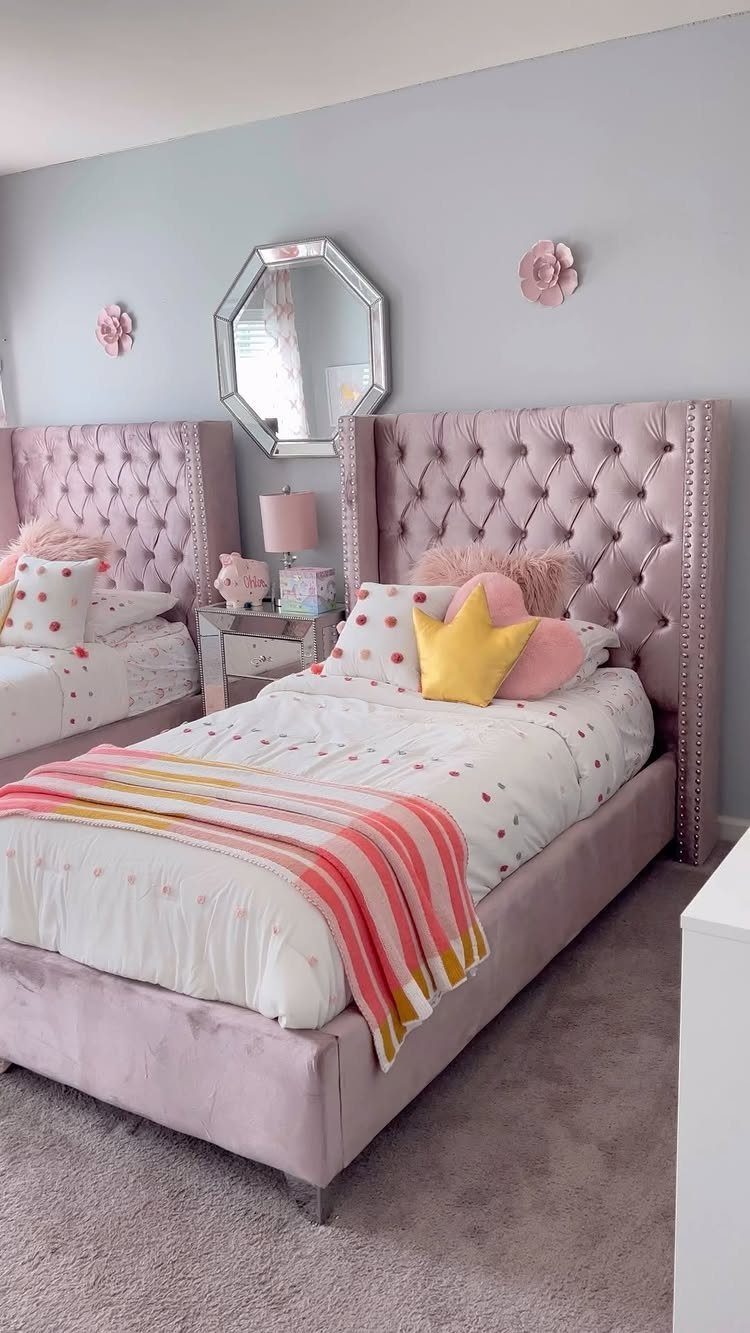 Two matching pink velvet tufted beds in a grey bedroom with mirrored furniture.