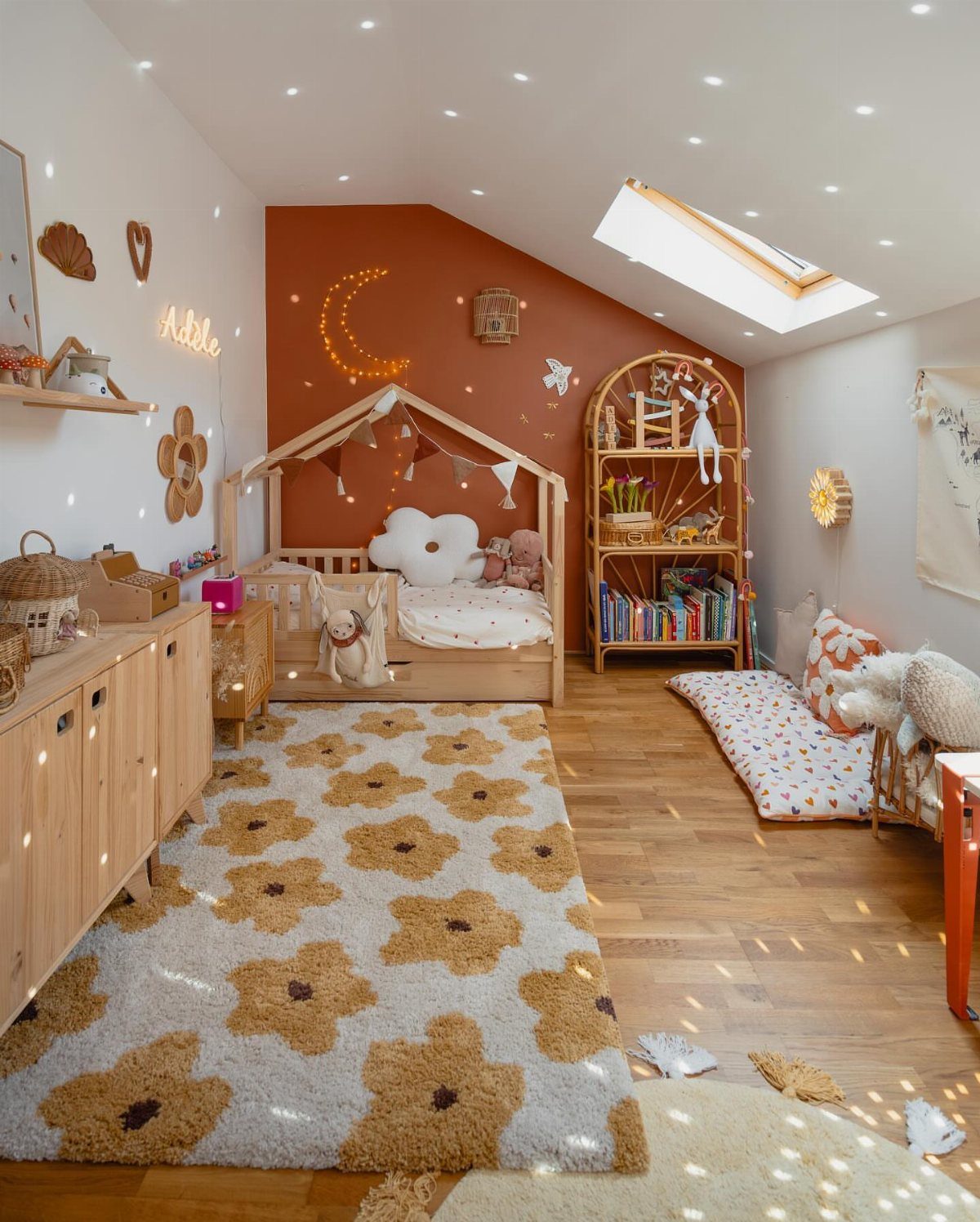 Terracotta accent wall in a toddler bedroom with a wooden house bed and floral rug.