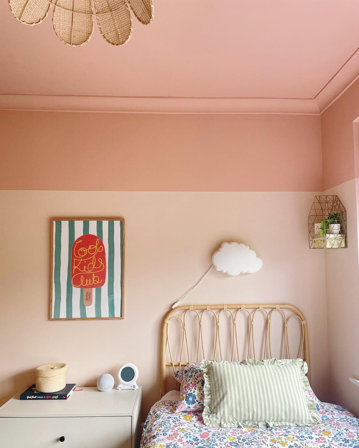 Two-tone pink walls in a toddler bedroom with a rattan headboard and floral bedding.